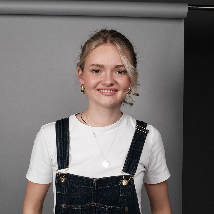 Portrait von Lina, Grafikdesign Studentin, sie trägt ein weißes tshirt mit einer blauen latzhose und lächelt